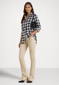 Károvaná košeľa v námorníckej modrej a bielej farbe, svetlo béžové zvonové nohavice a čierna kabelka. Modelka stojí s rukami vreckách, má na sebe čierne špicaté topánky.