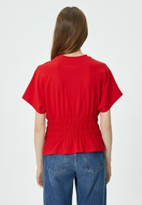 Top rosso a maniche corte con collo rotondo e vita arricciata; abbinato a jeans in denim blu con tasche posteriori e taglio dritto.