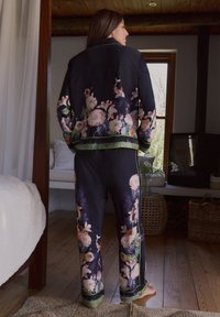 Completo pigiama floreale in raso blu navy, composto da giacca e pantaloni. Il design include vivaci motivi floreali e accenti in raso verde.
