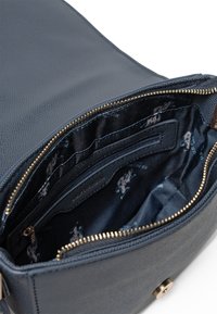 Interno di una borsa in pelle texturizzata blu navy con chiusura a zip. Presenta diverse tasche e una fodera in tessuto con motivo, completata da una zip in tonalità oro.