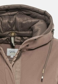 Chaqueta de plumas marrón con capucha acolchada, cordón y cierre de botón. Presenta costuras internas y etiqueta de marca en el cuello.
