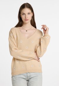 Beige kötött pulóver V-nyakkal, hímzett fehér virágokkal. bordás mandzsettákkal és aljjal, laza fazonnal, puha textúrával.