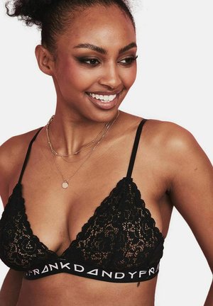 Bralette in pizzo nero con forma triangolare, bordi ondulati, spalline regolabili e fascia elastica con logo sulla parte inferiore.