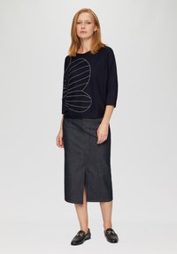 Granatowy sweter z białym wzorem graficznym, w połączeniu z ciemnoniebieską spódnicą midi z przodu z rozcięciem oraz czarnymi mokasynami ze złotym wykończeniem.