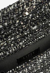 Čierna a strieborná kabelka z flitrového materiálu s textúrovaným tkaným dizajnom, s čiernym hodvábnym interiérom a viditeľnou značkovou etiketou.