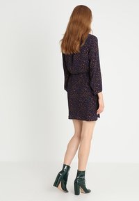 Granatowa sukienka w pomarańczowy kwiatowy wzór, z długimi rękawami i przewężoną talią. Połączona z zielonymi lakierowanymi botkami za kostkę.