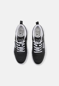 Baskets noires avec lacets blancs et semelles en caoutchouc. Présentent une tige en cuir lisse avec des perforations. Marque visible sur la languette et le côté.