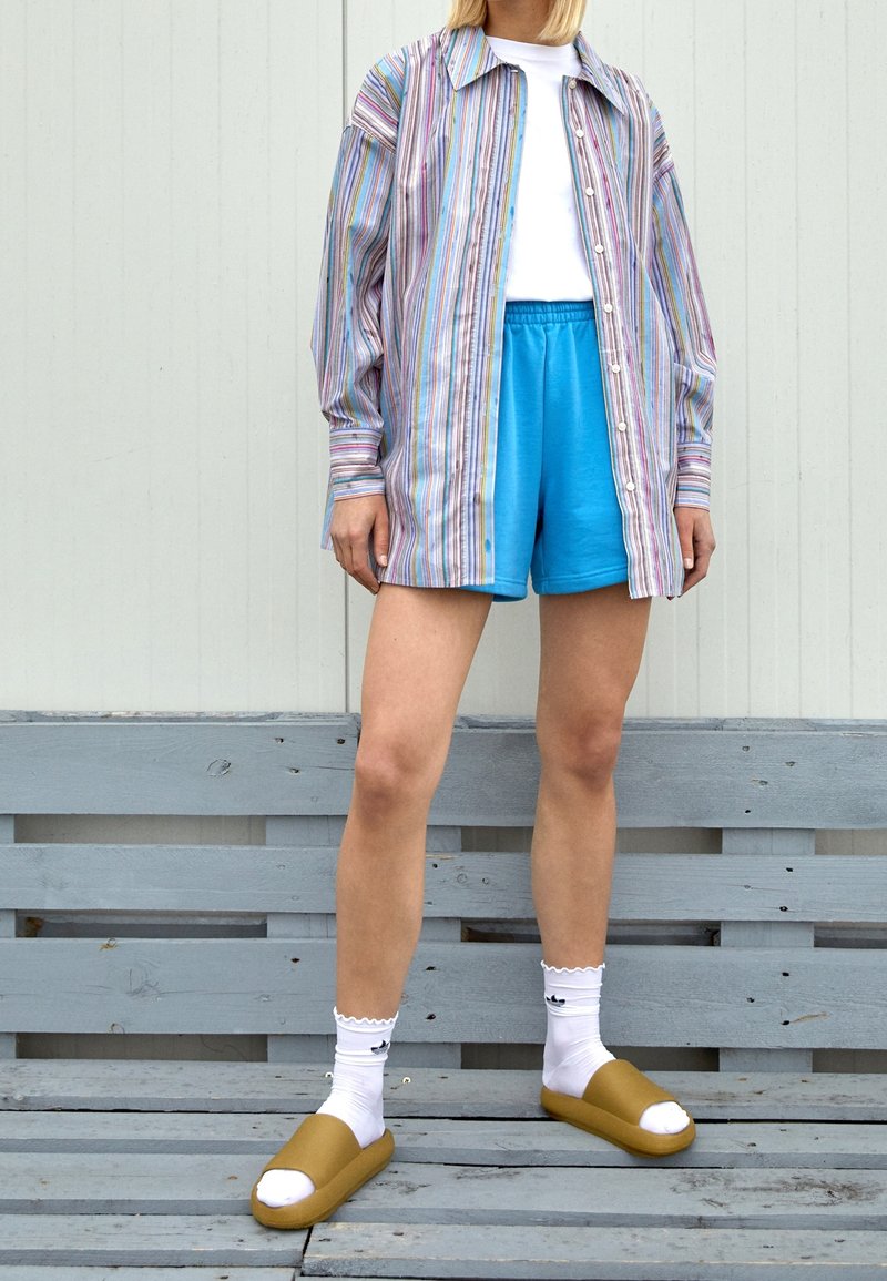 Randig, oversized skjorta med knappar i pastellfärger; matched med blå shorts, vita strumpor och bruna slides med öppen topp.