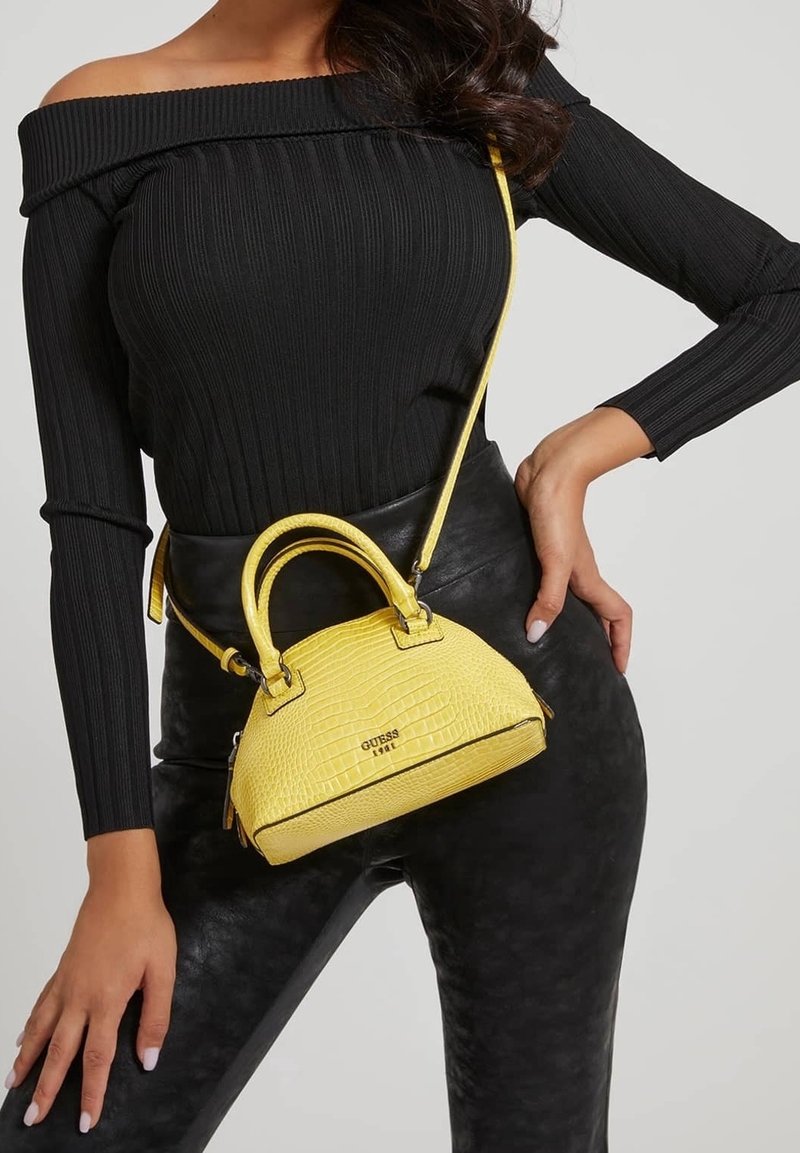 Gul håndtaske med krokodillemønster, struktureret design, runde håndtag og aftagelig rem, parret med en sort ribbet top og bukser.