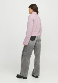 Pull rayé rose avec un col montant et une coupe courte, associé à un pantalon large gris avec un détail de poche contrastant.