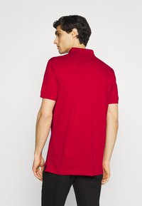 Rød polo t-shirt lavet af bomuld med korte ærmer, krave og sideslidser i kanten for nem bevægelse.