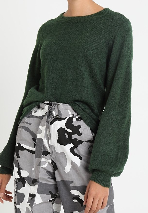Pull en maille vert foncé avec un col rond et des manches amples, assorti à un pantalon gris et blanc à motif camouflage avec une taille ceinturée.