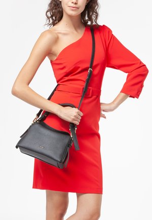 Borsa a mano in pelle nera con finitura textured, caratterizzata da una forma strutturata, manici doppi e una tracolla regolabile. Indossata con un vestito rosso.