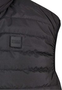 Černá péřová vesta s prošívanou texturou, s logem čtvercového štítku "URBAM CLASSICS" na přední straně.