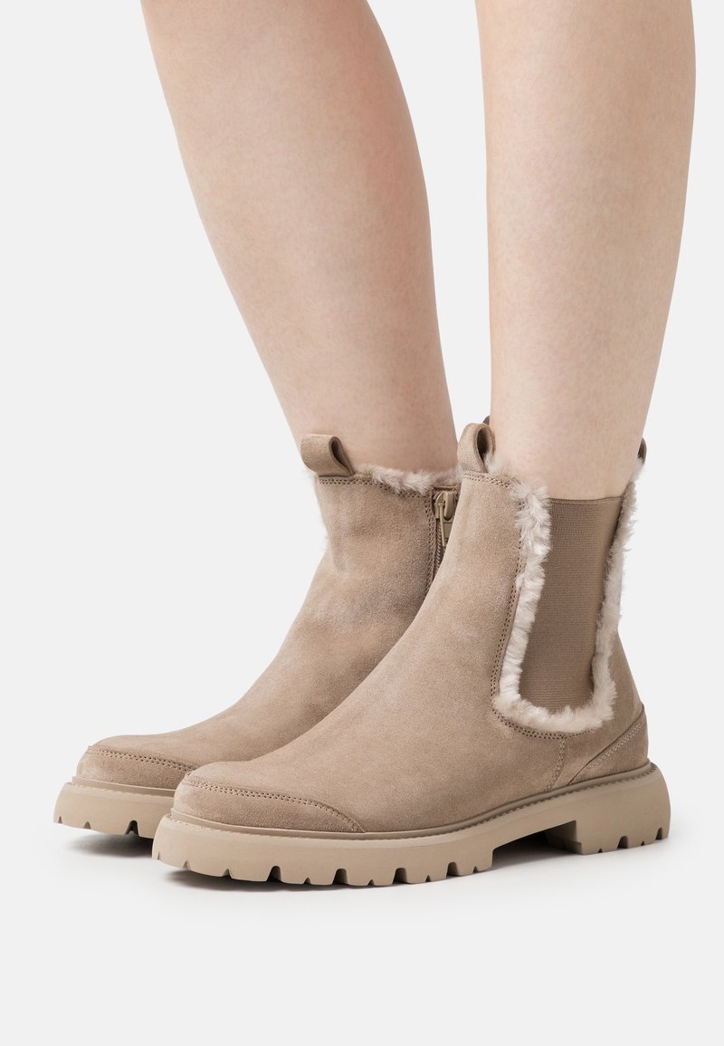 Bottes cheville en daim camel avec doublure en fausse fourrure et panneaux latéraux élastiques. Semelles épaisses en caoutchouc avec adhérence texturée. Fermeture éclair latérale.