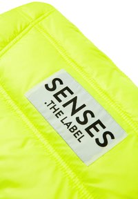 Neon-gelbe Pufferjacke mit einem rechteckigen Etikett, auf dem in fettem Schwarz "SENSES .THE LABEL" steht, das das gesteppten Design hervorhebt.