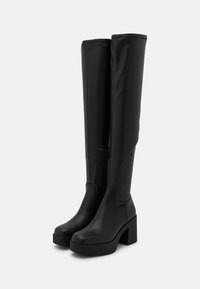 Botas negras hasta la rodilla hechas de suave cuero sintético, con un tacón cuadrado y una cremallera lateral para facilitar su uso. Detalle de costura sutil.