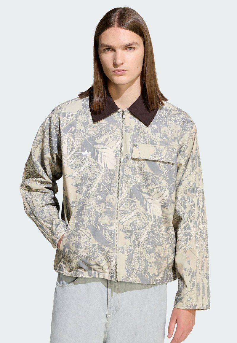 Camo-Muster Jacke in Beige und Grau mit braunem Kragen, durchgehendem Reißverschluss und einer Brusttasche. Hergestellt aus weichem, strukturiertem Stoff.