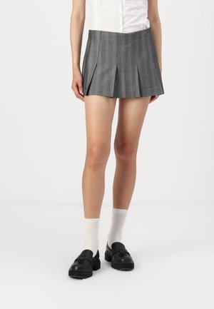 Halli hallidegusskurk, millel on vertikaalsed pinstribad ja mis on valmistatud tekstuurilisest kangast. Kombineeritud mustade loafers'itega ja valgetega lühikeste sokkidega.