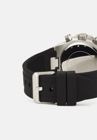 Musta silikoonkellarihm, millel on hõbedane metallist pandla ja sile tekstuur; omaduste hulka kuulub tekstureeritud muster sisepoolel mugavuse tagamiseks.