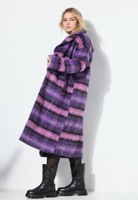 Lange wollen jas met paarse en roze horizontale strepen, oversized kraag en zwarte knopen. Gecombineerd met zwarte kniehoge laarzen.