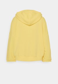 Sudadera amarilla con capucha, mangas largas, ajuste relajado, ribete acanalado y tejido suave de mezcla de algodón. Vista trasera que muestra detalles mínimos.