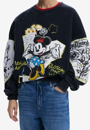 Sweatshirt met kleurrijke Minnie Mouse-afbeelding, madeliefjes, handgeschreven tekst en bloemenpatronen op een zwart-witte achtergrond, gedragen met blauwe jeans.