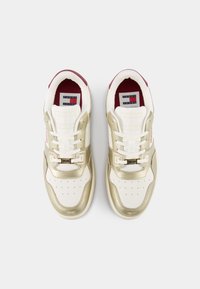 Paire de baskets blanches et or métallisé avec des lacets blancs et une doublure intérieure bordeaux, vue de dessus sur un fond uni.