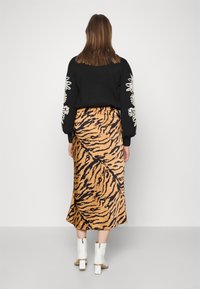Pull noir avec broderies florales sur les manches, associé à une jupe midi à rayures tigre marron et des bottines à talons épais blanches.