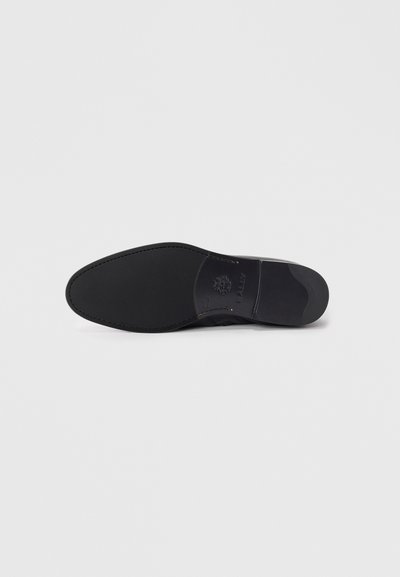 Suela de zapato negra con una textura suave, banda de rodadura de goma y logotipo en relieve. Forma ligeramente redondeada con una sección de tacón estrecha.