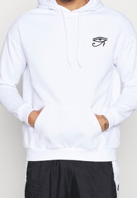 Felpa bianca con cappuccio con coulisse, tasca frontale e simbolo degli occhi neri sul petto a sinistra. Tessuto liscio con polsini e orlo a coste.