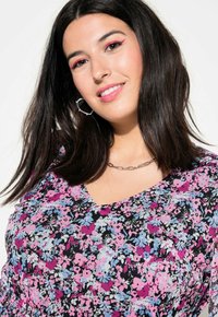 Robe florale sur fond noir, ornée de fleurs roses et bleues, au design en V et à la texture froncée. Collier en chaîne argentée et boucles d'oreilles créoles.