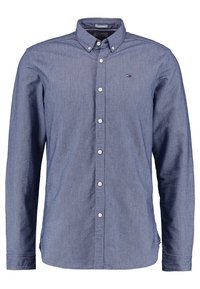 Camisa de botones en tela chambray azul oscuro, con cuello esparcido, mangas largas y botones blancos. Detalle de logo pequeño en el pecho.