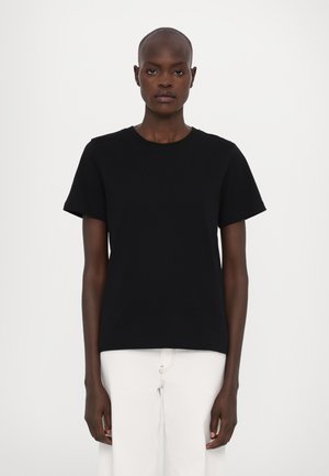 Black short-sleeve t-shirt in cotton fabric with a round neckline, displayed on a model against a plain white background.