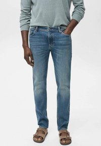 Blauwe spijkerbroeken met een rechte snit,Featuring een vervaagde wassing en vijf zakken. Gedragen met bruine sandalen en een lichtgrijze blouse met lange mouwen.