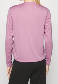 Långärmad topp i texturerad ljuslila tyg, med rund halsringning och avslappnad passform. Bar med svarta byxor, visad från bakvyn.