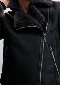 Czarna skórzana kurtka z miękkim szarym futerkiem przy kołnierzu, z metalowymi suwakami i starannym przeszyciem. Strukturalny design z bocznymi kieszeniami.