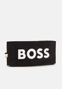 Juodas zomšinės piniginės su dideliu baltu "BOSS" logotipu. Pasižymi lygiu paviršiumi, švariu dizainu ir mažu auksiniu bei dryžuotu detaliu akcentu.