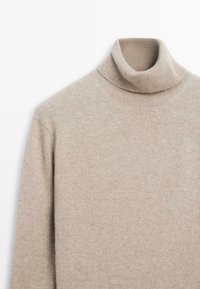 Maglione a collo alto beige realizzato in morbido tessuto a maglia, con colletto a coste e maniche lunghe dalla trama liscia.