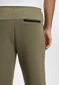 Oliwkowo-zielone dresy z miękkiego materiału o dopasowanym kroju, z małą czarną kieszonką z tyłu i gładką gumką w pasie.