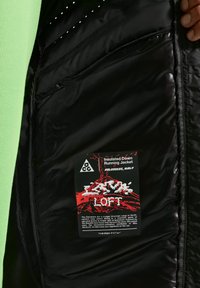 Εσωτερικό μαύρου μονωτικού μπουφάν που δείχνει το λογότυπο ACG, την ετικέτα AeroLoft με κόκκινο γραφικό βουνού και περιγραφή της έμπνευσης πεζοπορίας στα Δολομίτες.