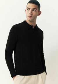 Musta pikaeungsõlvaga polo särk, mis on valmistatud kudumiskangast. Särgil on klassikaline krae, kolme nööbiga kinnitamine ja soonikkoes mansetid. Kannab heledate pükstega.