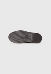 Black rubber sneaker sole with distinctive wave-patterned tread and logo detail. Flat shape with textured surface for grip.