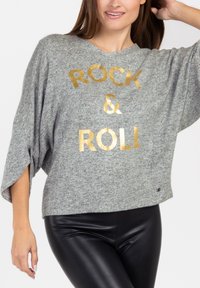 Maglione grigio oversize con testo metallizzato dorato "ROCK & ROLL" sul davanti. Tessuto morbido e dalla texture, con maniche larghe e orlo arrotondato.