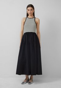 Gestreifter Tank-Top mit schwarzem, schwingendem Rock. Das Kleid verfügt über Taschen und ist aus leichtem Stoff gefertigt. Silberne Schuhe vervollständigen den Look.