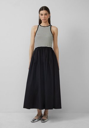 Gestreepte tanktop met zwarte vloeiende rok. De jurk heeft zakken en is gemaakt van lichte stof. Zilveren schoenen maken de look compleet.