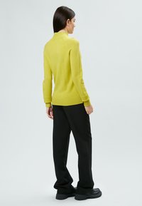 Maglione giallo brillante a maniche lunghe con orlo e colletto a coste, abbinato a pantaloni neri a gamba larga e scarpe nere spesse. Texture liscia.