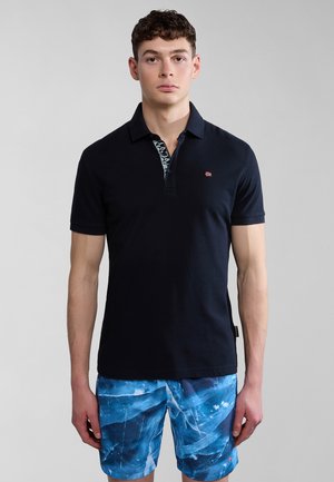 Polo navy con una patta decorata e un piccolo logo. Indossato con pantaloni corti blu con un design marmorizzato in tonalità più chiare.