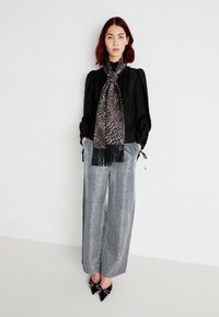 Blusa nera a maniche lunghe, pantaloni larghi grigi a pieghe e una sciarpa leopardata con frange. Scarpe nere a punta con decorazioni.