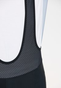 Nahaufnahme von schwarzen Mesh-Radträgerhosen mit weißem, atmungsaktivem Jersey darunter, die Textur und Nähte hervorheben.